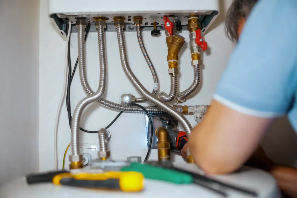 Engineer assessing boiler pipework and connections to determine if boiler repair or replacement is needed