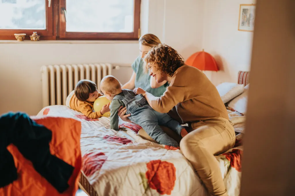 A joyful moment of a family playing with their children on a bed in a warm, inviting environment, emphasising family bonds and care in a warm environment