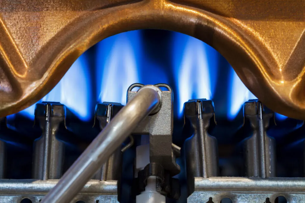 The fire burns in the modern water heater without cover. Closeup, selective focus - a boiler with high efficiency will have a blue flame