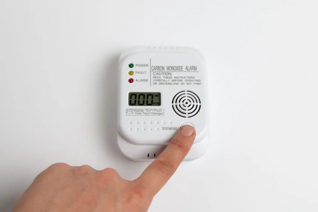 Carbon monoxide alarm on a white background with a hand pressing the test button