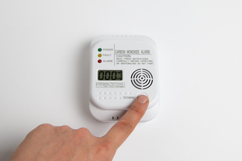 Carbon monoxide alarm on a white background with a hand pressing the test button