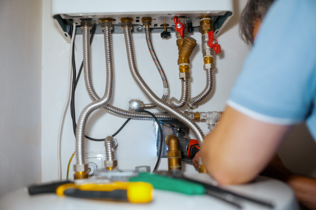 Engineer assessing boiler pipework and connections to determine if boiler repair or replacement is needed