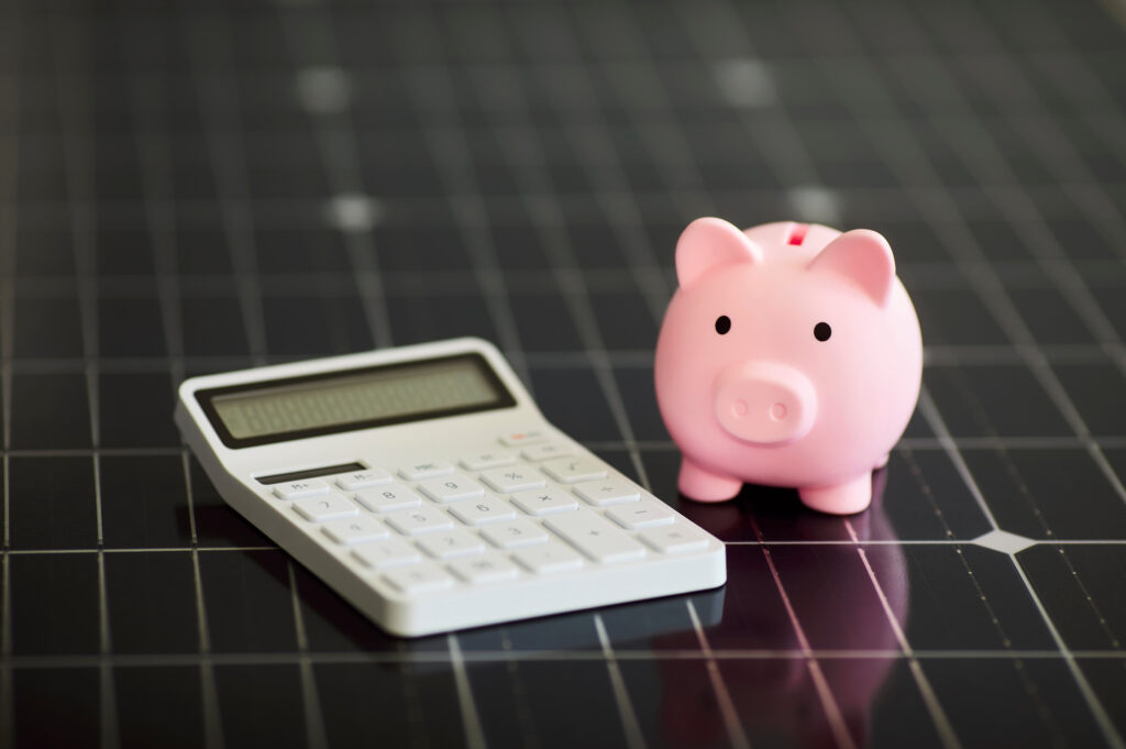 Calculator and pink piggy bank on modern black photovoltaic solar panel.